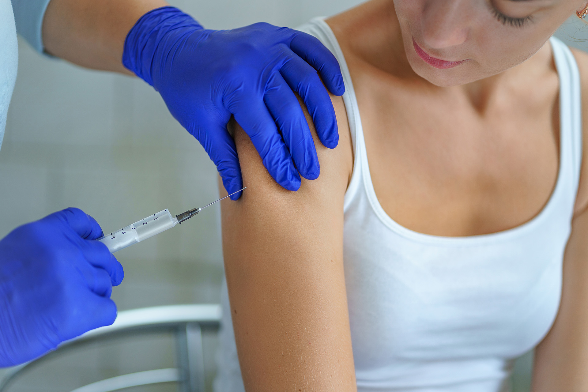 mani di medico con guanti in lattice blu che fa un'iniezione al braccio di una paziente